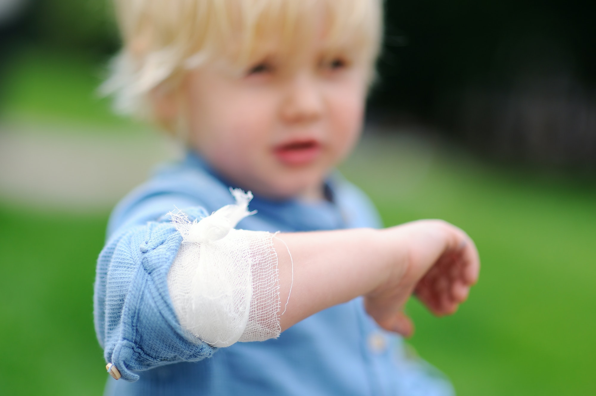 Cute little boy looking on his elbow with applied bandage. Child first aid.