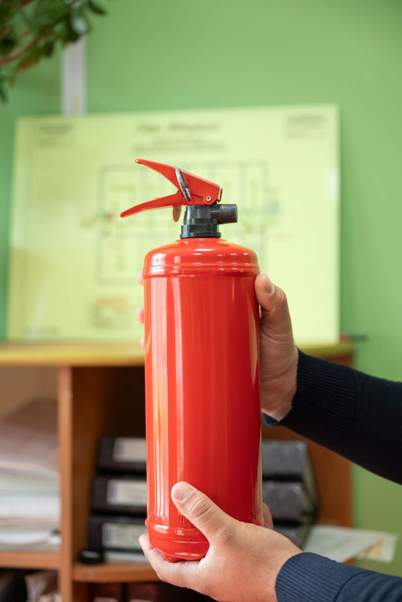 man holds a fire extinguisher in his hands against the background of a fire evacuation plan.